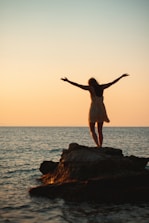 woman in white dress standing on rock formation near sea during daytime