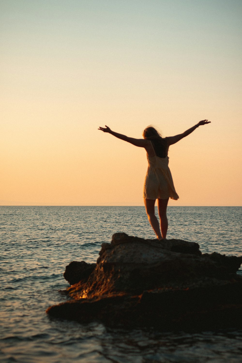 woman in white dress standing on rock formation near sea during daytime