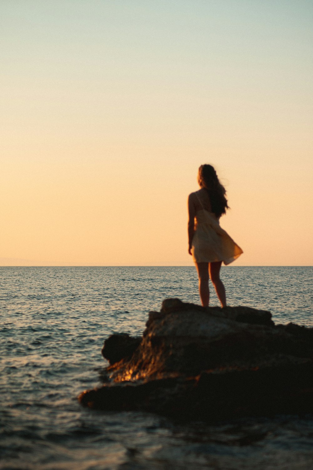 woman in white dress standing on rock near sea during daytime