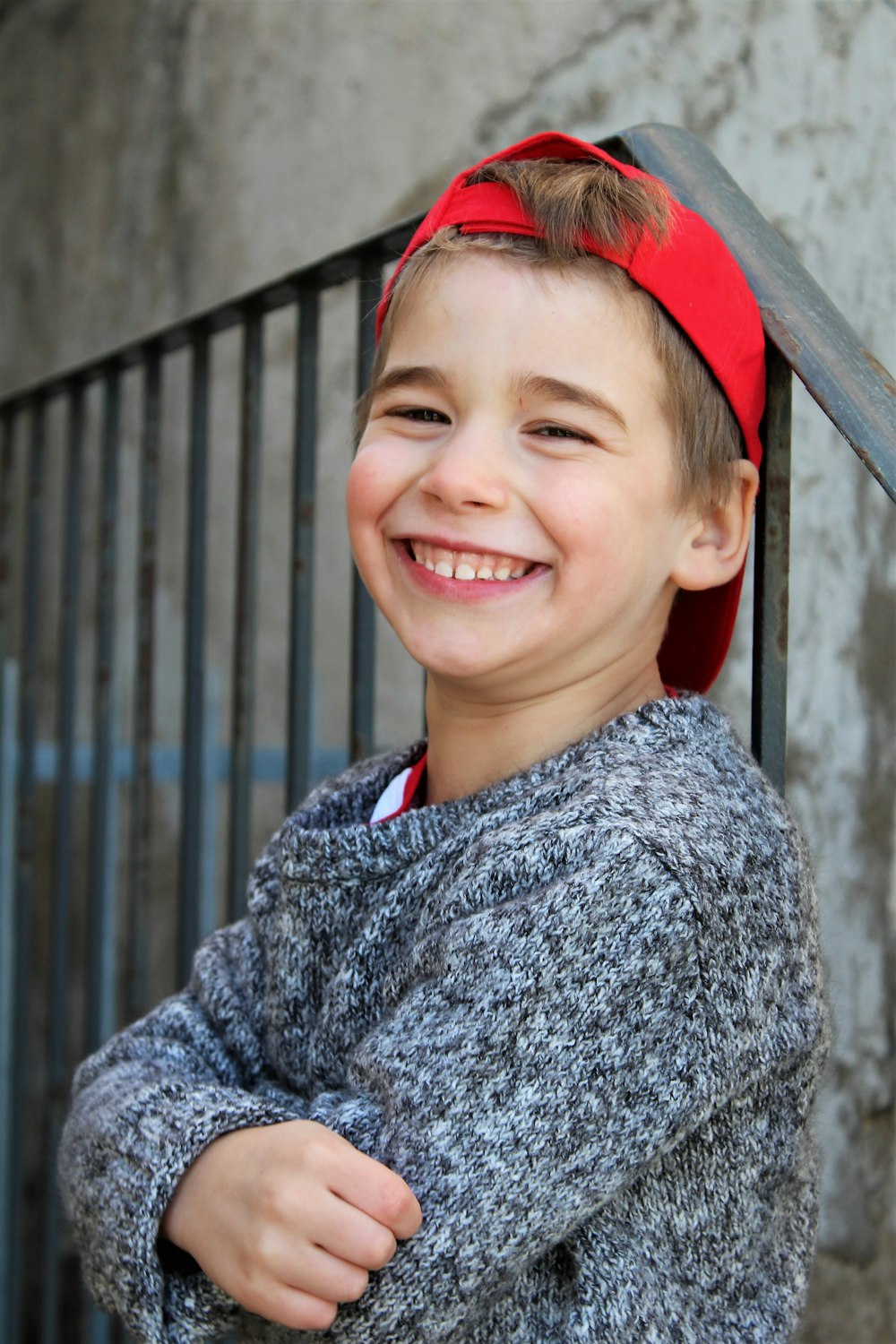 smiling boy in gray and black sweater wearing red cap