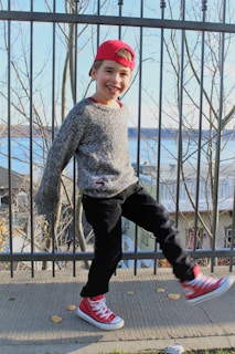 A child wearing a cozy gray sweater and playful sneakers, running through a park in autumn.