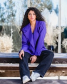 woman in purple blazer sitting on brown wooden bench during daytime