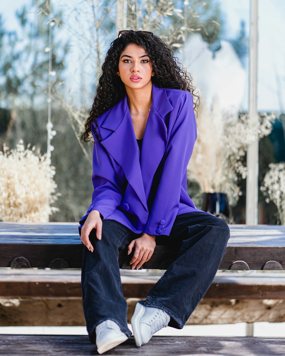 woman in purple blazer sitting on brown wooden bench during daytime