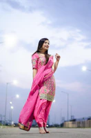 A woman in a vibrant shalwar kameez standing by a Stockholm waterfront at sunset.