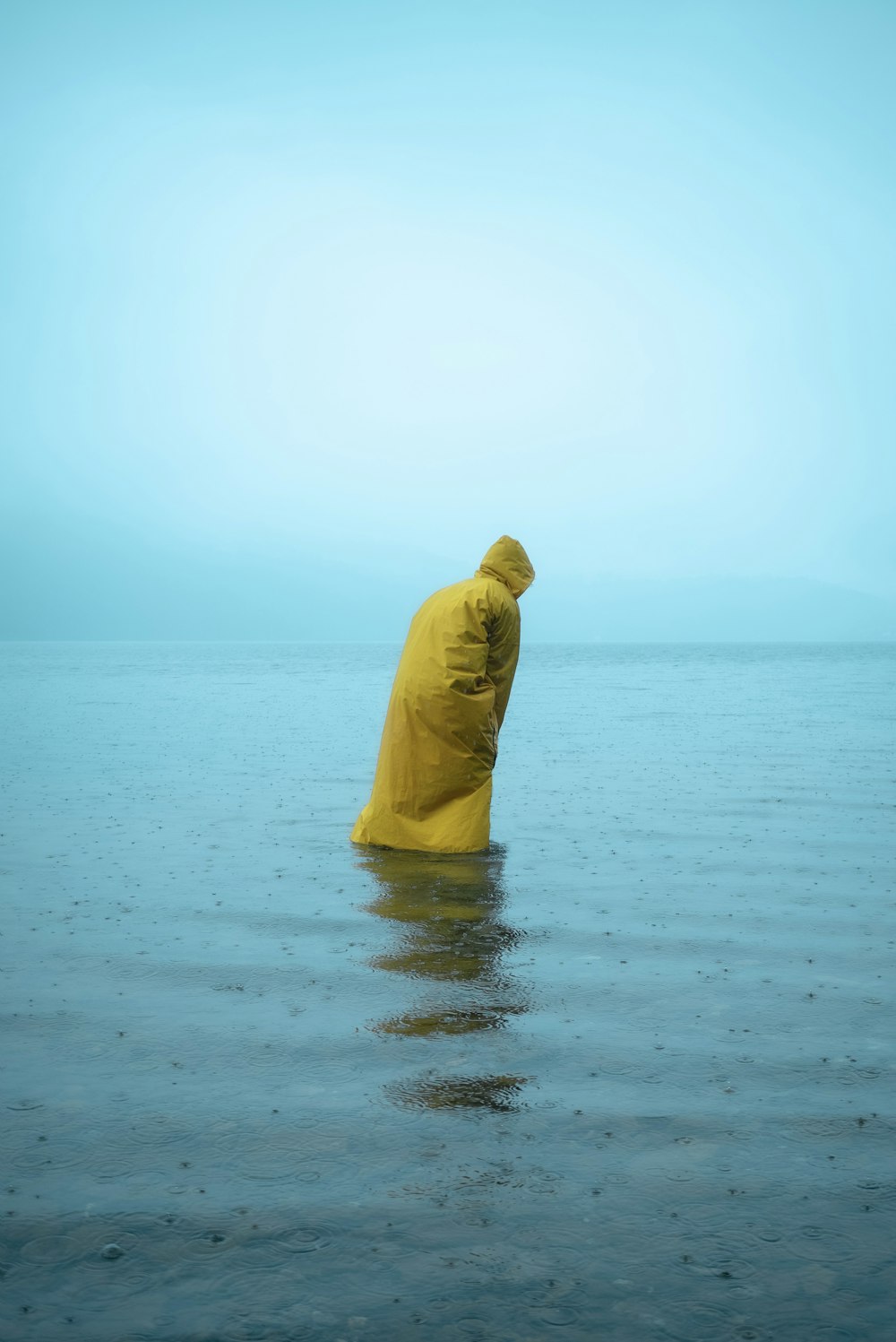 pessoa em capuz amarelo em pé na costa do mar durante o dia