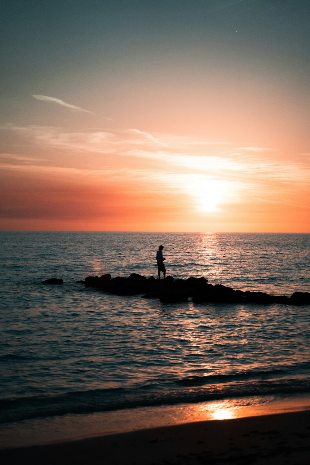 silhouette of people on rock formation in the middle of sea during sunset