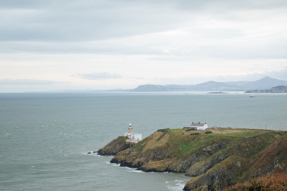 Phare blanc sur une colline couverte d’herbe verte au bord de la mer sous des nuages blancs pendant la journée