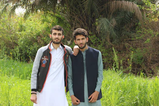 Two brothers standing in a lush green Irish field, cameras in hand, smiling warmly under a soft cloudy sky.