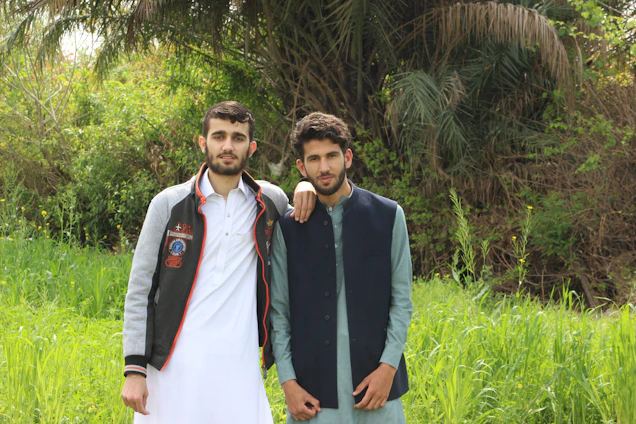 Two brothers standing in a lush green Irish field, cameras in hand, smiling warmly under a soft cloudy sky.