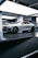 A sleek, silver sports car is parked inside a modern, well-lit showroom. The car features prominent aerodynamic lines, large black alloy wheels, and a distinctive front grille. The lighting in the room highlights the car’s glossy finish, and the minimalist design of the surroundings complements the high-tech appearance of the vehicle.