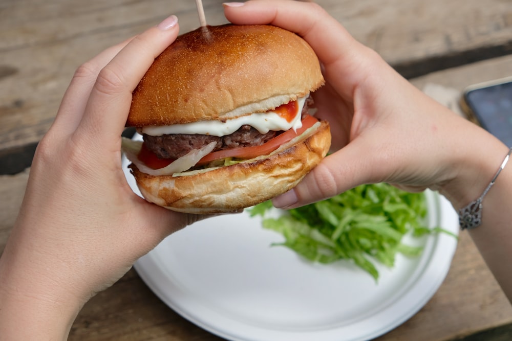 person holding burger with lettuce and tomato