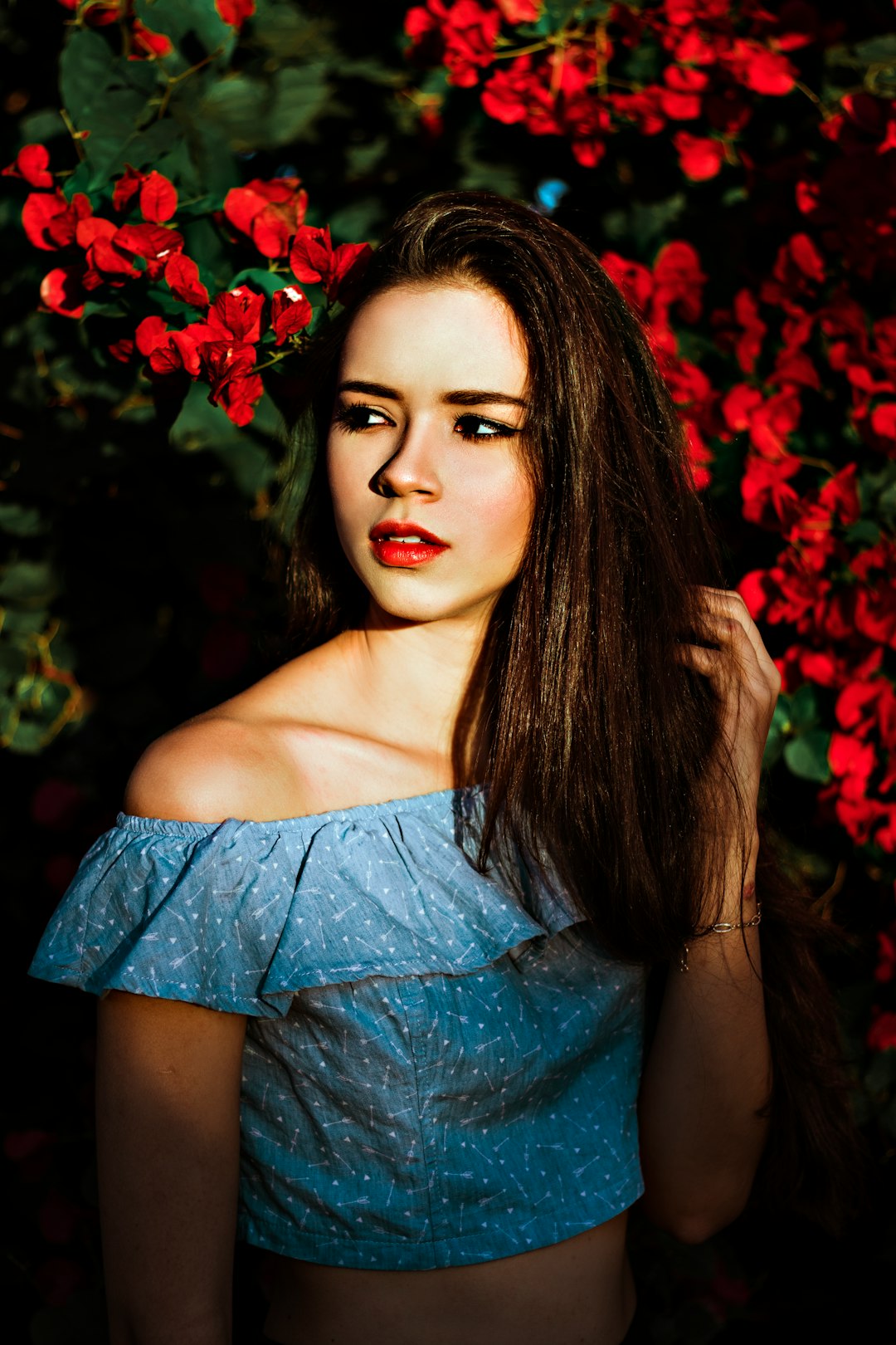 woman in blue off shoulder dress standing beside red flowers