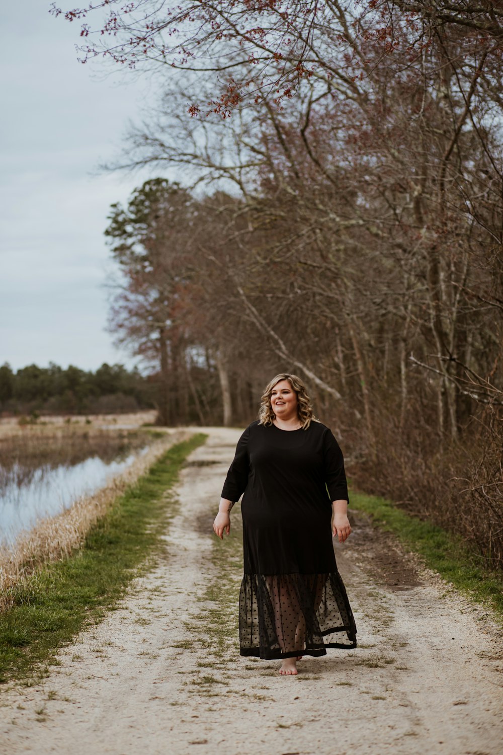 woman in black long sleeve dress standing on brown dirt road near river during daytime