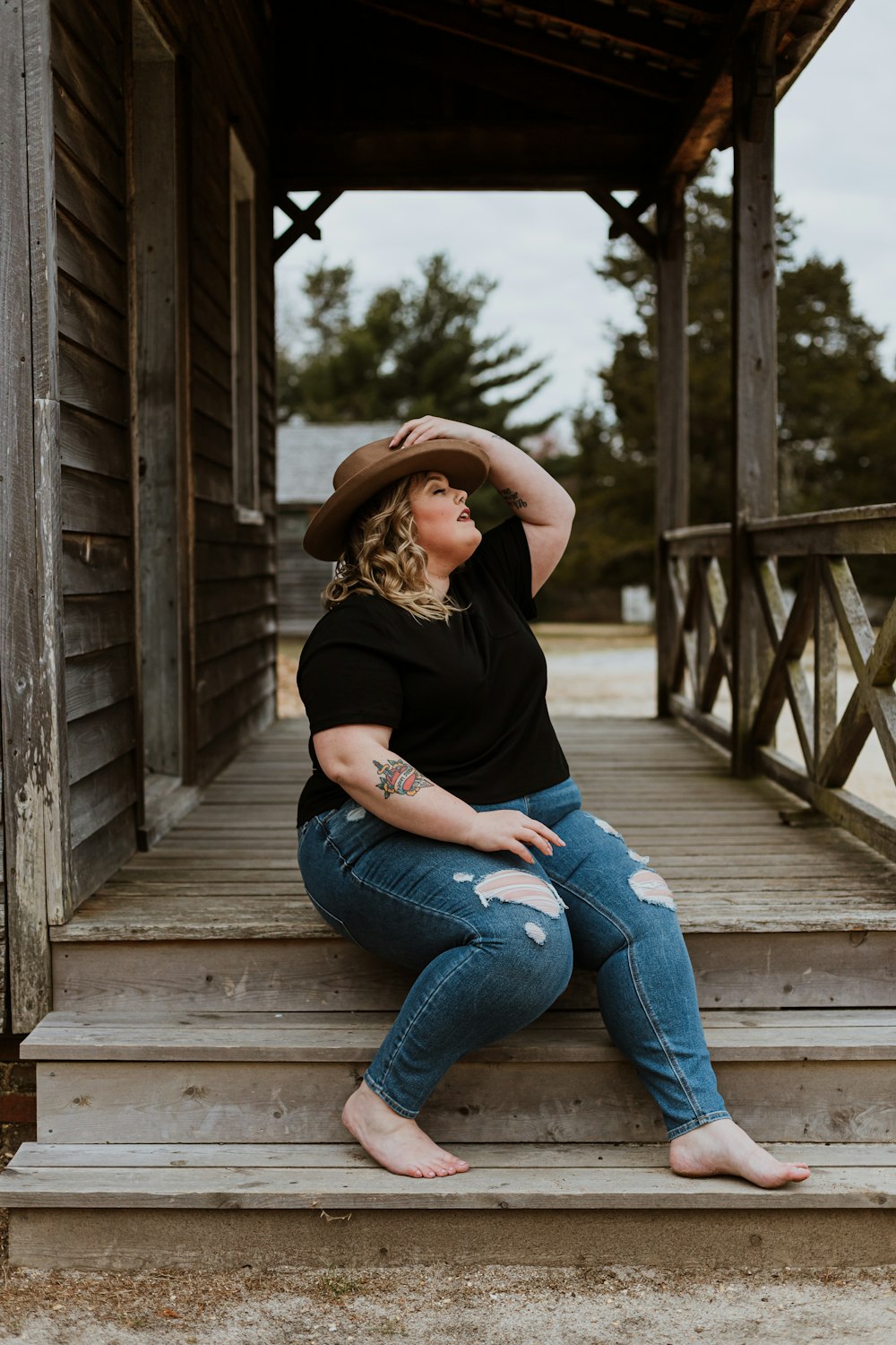 woman in black t-shirt and blue denim jeans sitting on wooden bridge