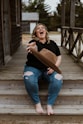 woman in black shirt and blue denim jeans sitting on wooden bridge