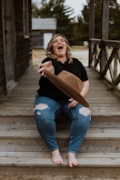 woman in black shirt and blue denim jeans sitting on wooden bridge