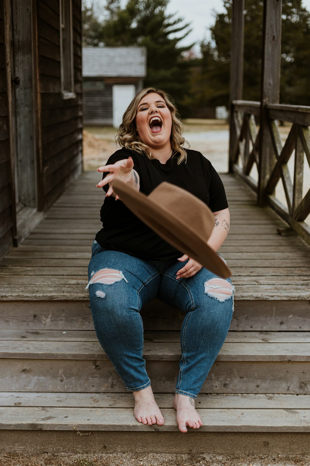 woman in black shirt and blue denim jeans sitting on wooden bridge