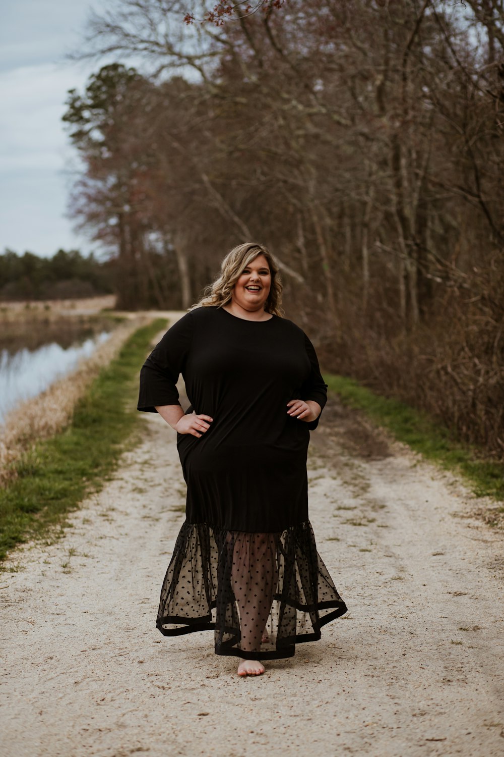 woman in black long sleeve dress standing on gray road near river during daytime