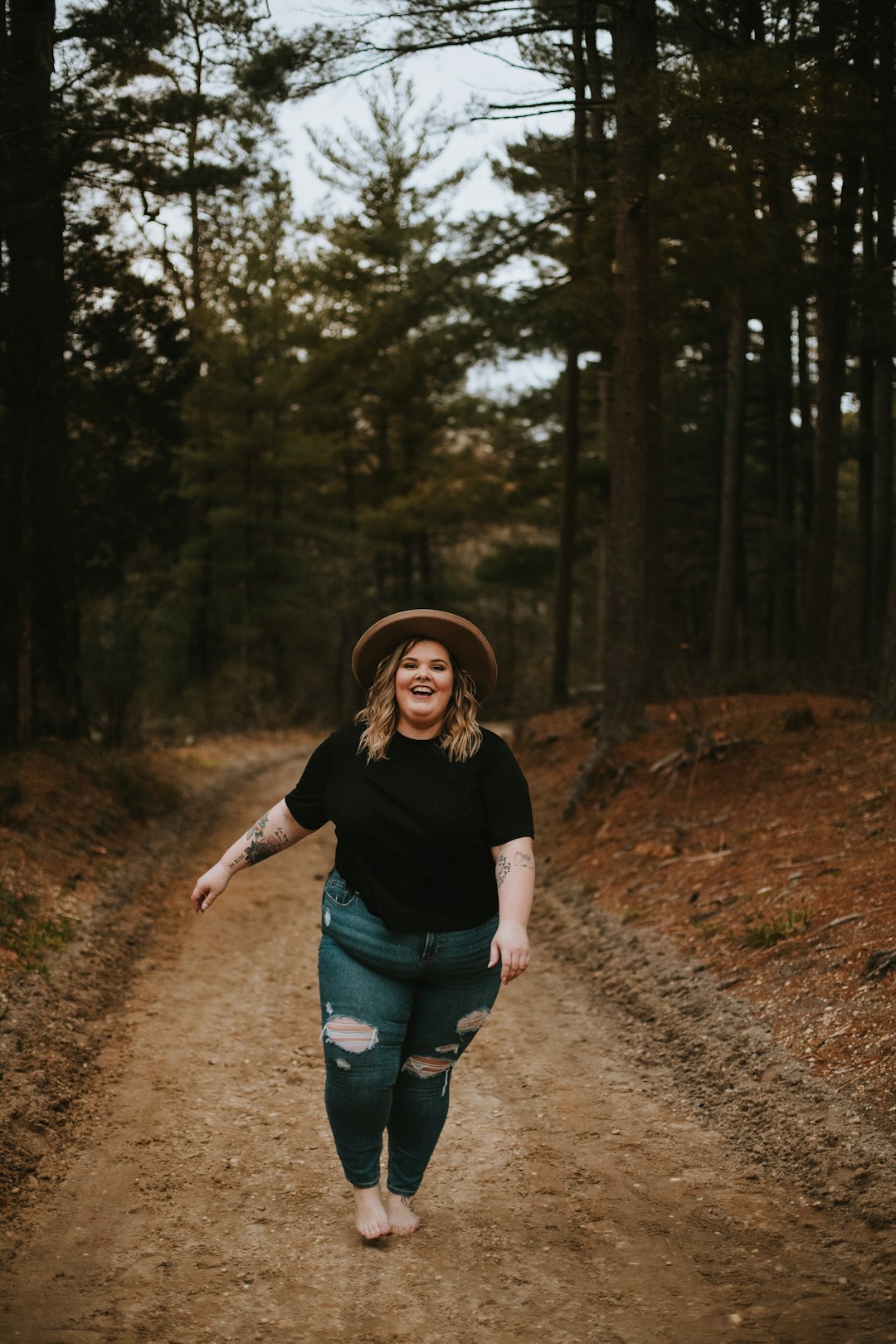 woman in black t-shirt and blue denim shorts standing on dirt road between trees during