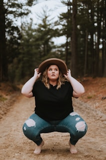 woman in black tank top and blue denim jeans sitting on ground surrounded by trees during