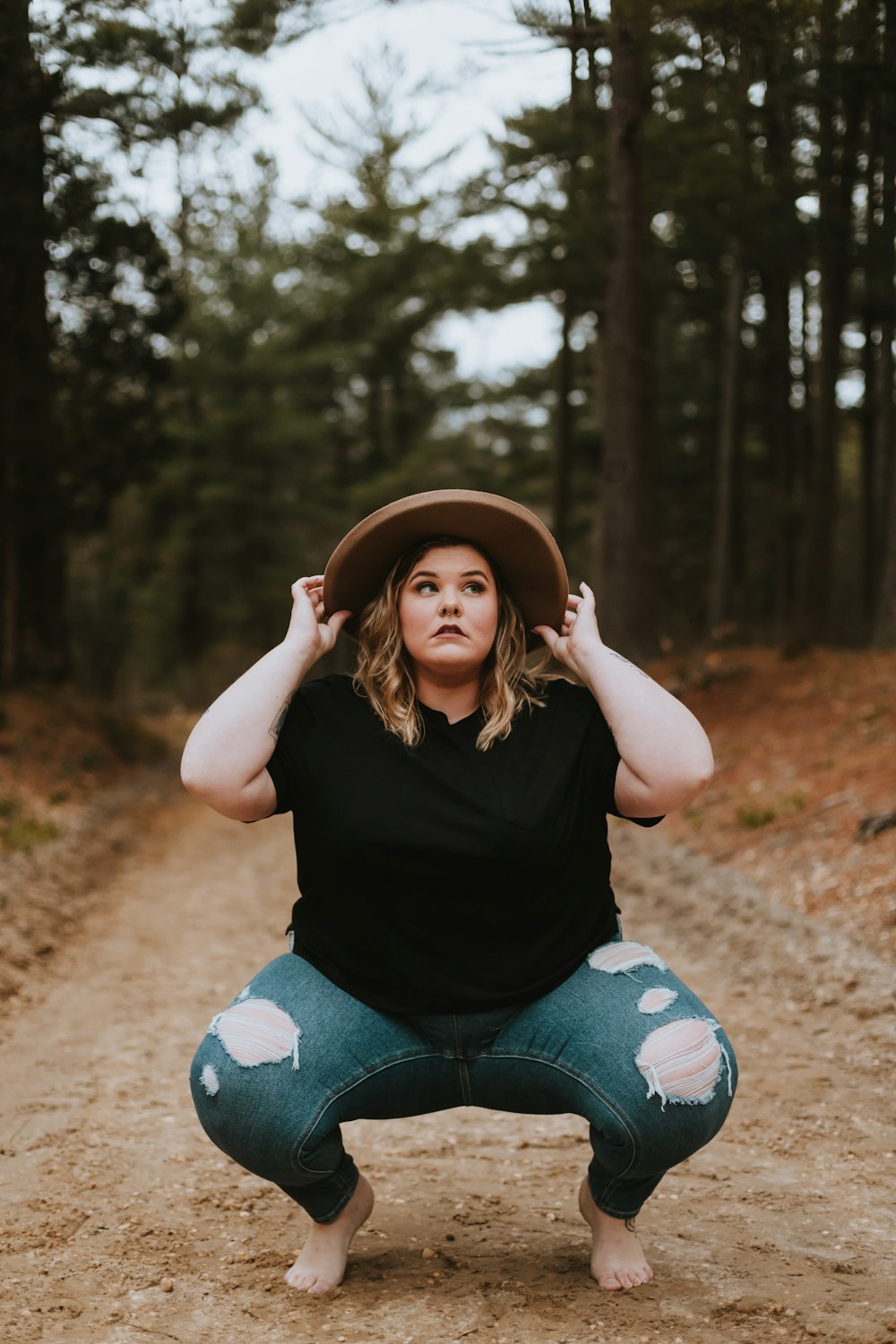 woman in black tank top and blue denim jeans sitting on ground surrounded by trees during