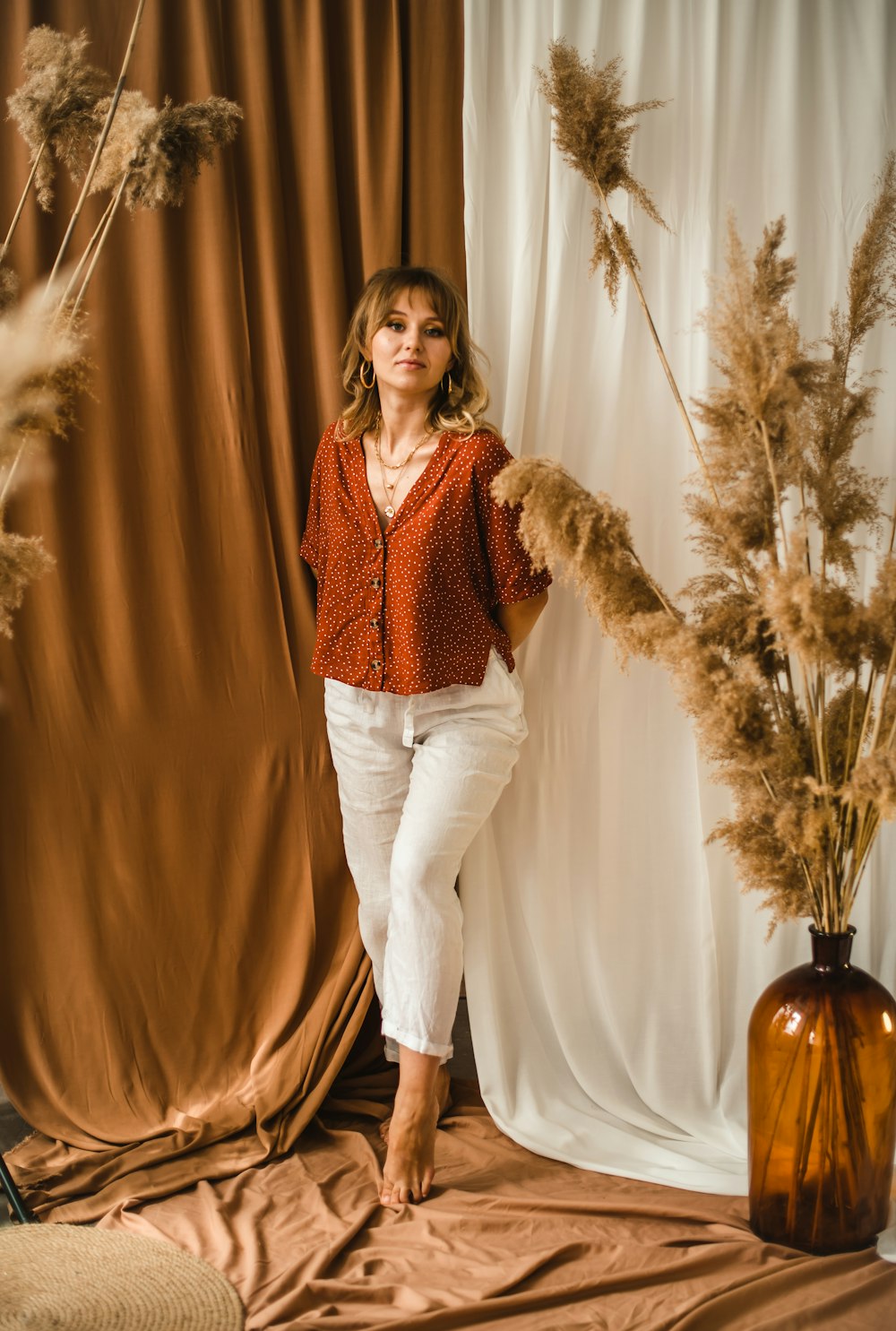 woman in red sweater and white pants standing beside green plant