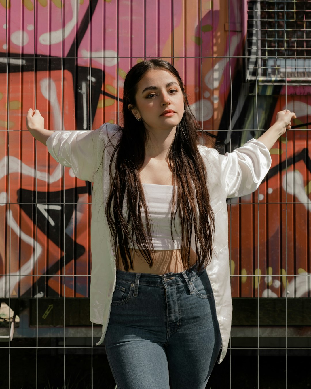 woman in white blazer and blue denim jeans standing beside black metal fence