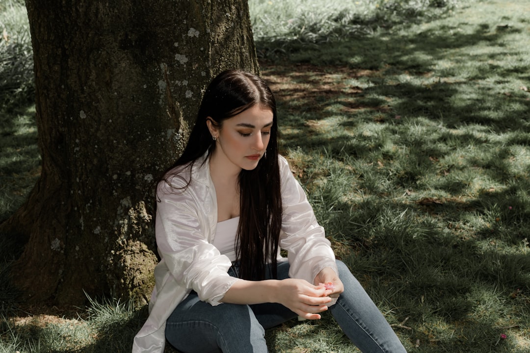 woman in white long sleeve shirt and blue denim jeans sitting on green grass field beside