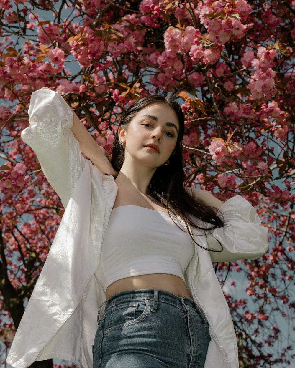 woman in white off shoulder shirt and blue denim jeans standing beside red flowers
