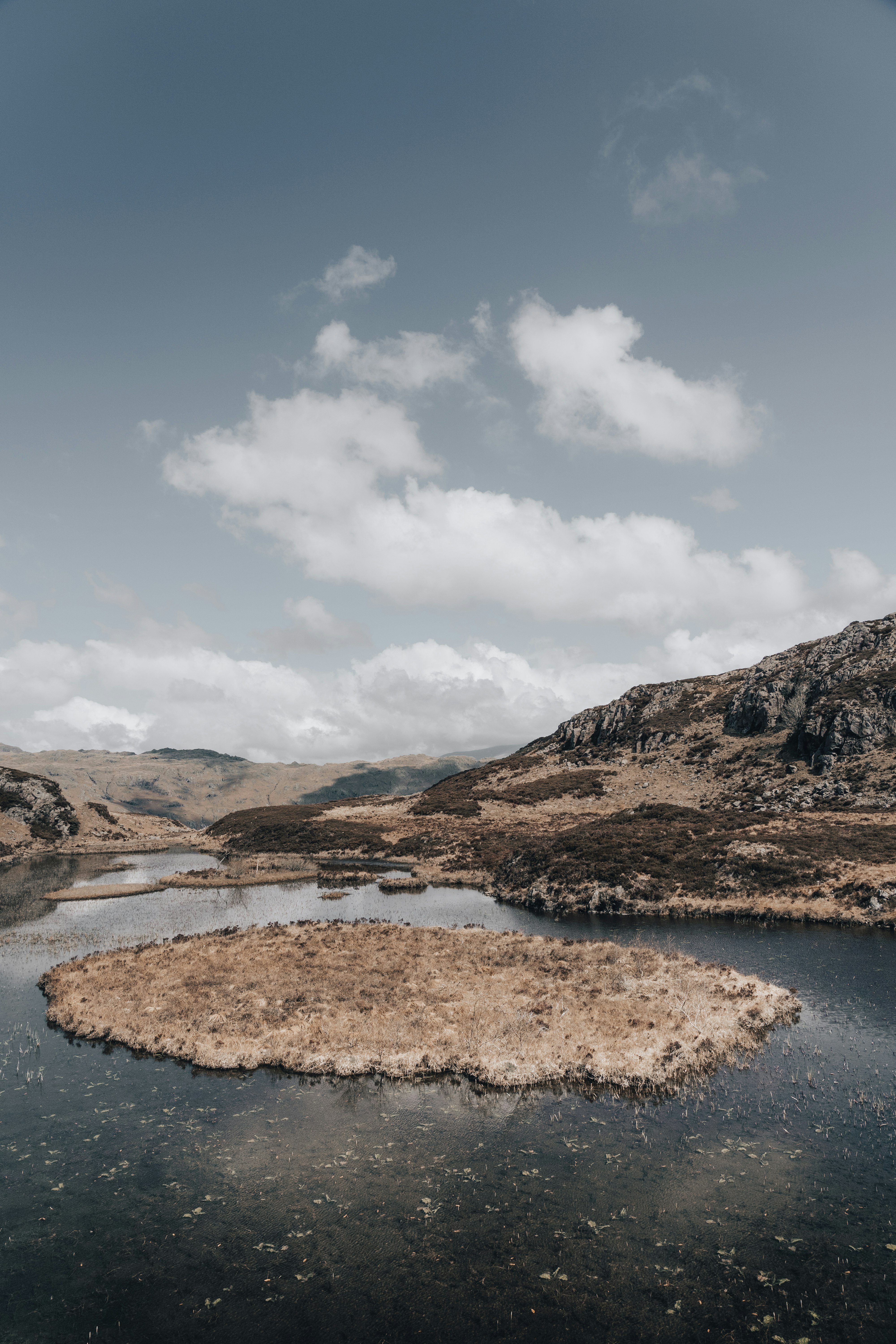 brown and green mountains beside river under white clouds and blue sky during daytime