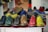 A collection of colorful leather dress shoes is arranged on a tabletop. The shoes come in various vibrant colors, including green, yellow, brown, red, and blue. They feature classic brogue detailing and are neatly aligned in rows, creating an eye-catching display.