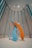 A modern art sculpture consisting of large, abstract brush strokes in vibrant blue and orange hues. The sculpture is set in a spacious room with high ceilings and vertically aligned, louvered wall panels. The lighting is soft, casting gentle shadows on the floor.