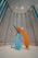 A modern art sculpture consisting of large, abstract brush strokes in vibrant blue and orange hues. The sculpture is set in a spacious room with high ceilings and vertically aligned, louvered wall panels. The lighting is soft, casting gentle shadows on the floor.
