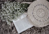 A delicate bouquet of wildflowers in soft blues and creams resting beside a life glow workbook on a rustic wooden surface.