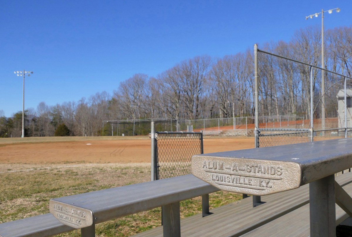 Wooden bench by a metal fence, suggesting a meeting spot for youth sports team sign-ups and volunteer coordination.