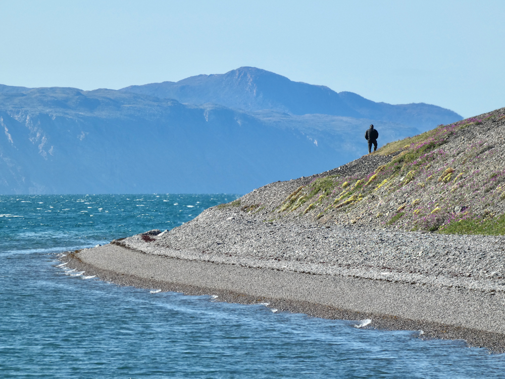 person in black jacket sitting on gray concrete pavement near body of water during daytime