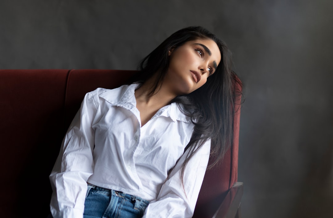 woman in white dress shirt and blue denim jeans sitting on red couch