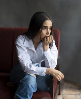 woman in white dress shirt and blue denim jeans sitting on red couch