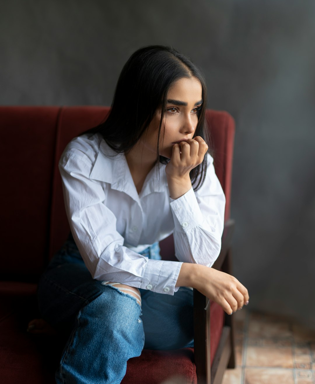 woman in white dress shirt and blue denim jeans sitting on red couch