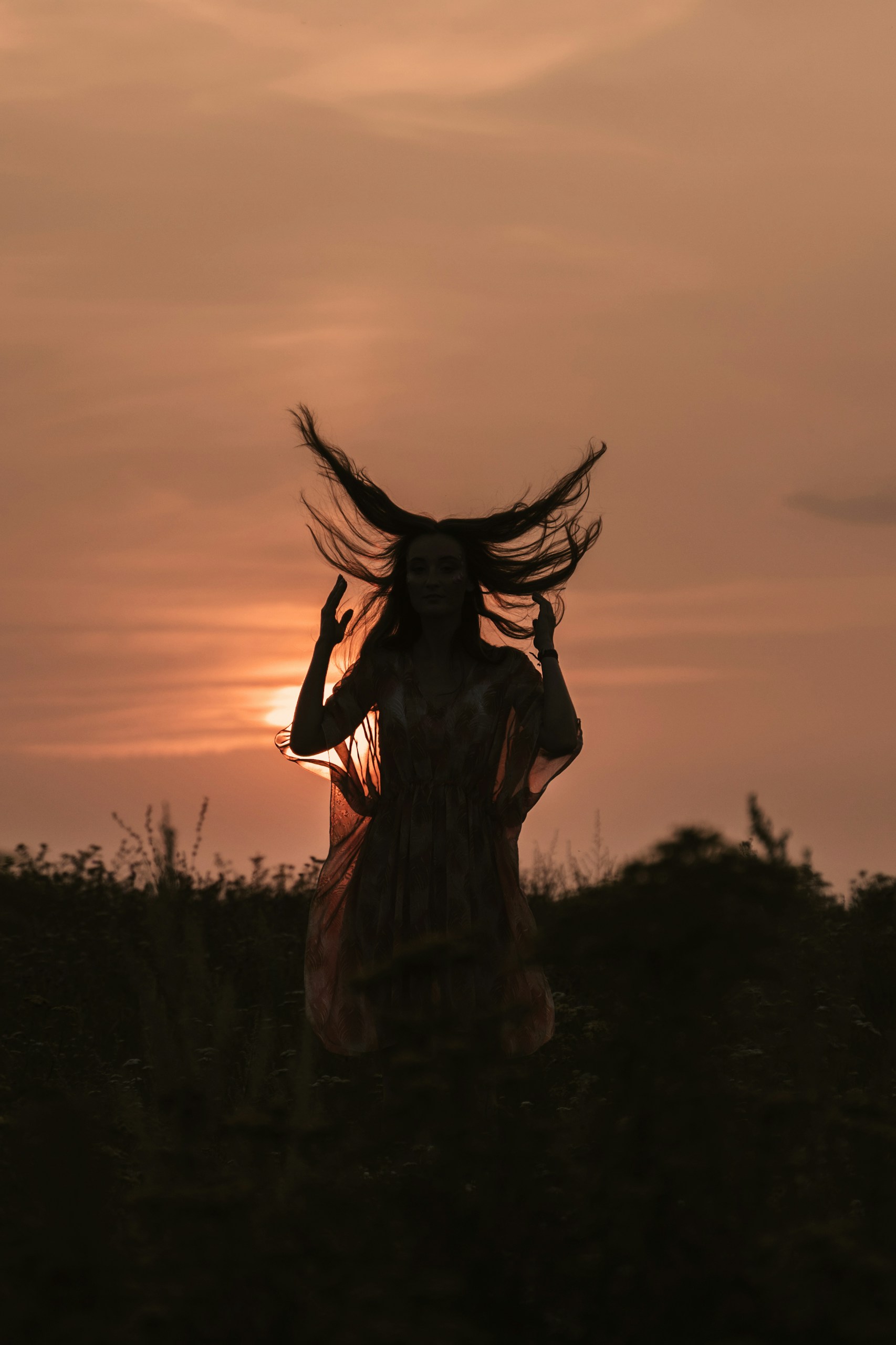 woman in black dress standing on green grass field during sunset