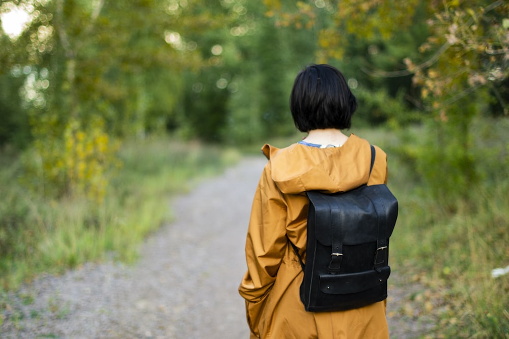woman in black leather backpack walking on pathway during daytime
