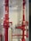 Two large red industrial pipes with pressure gauges and valves are mounted on a utility wall. The pipes have labels with numbers and are connected to other smaller pipes and devices.