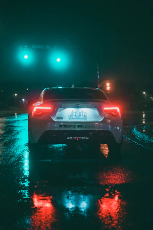 A car waiting patiently curbside on a rainy evening, its lights reflecting softly on wet pavement.
