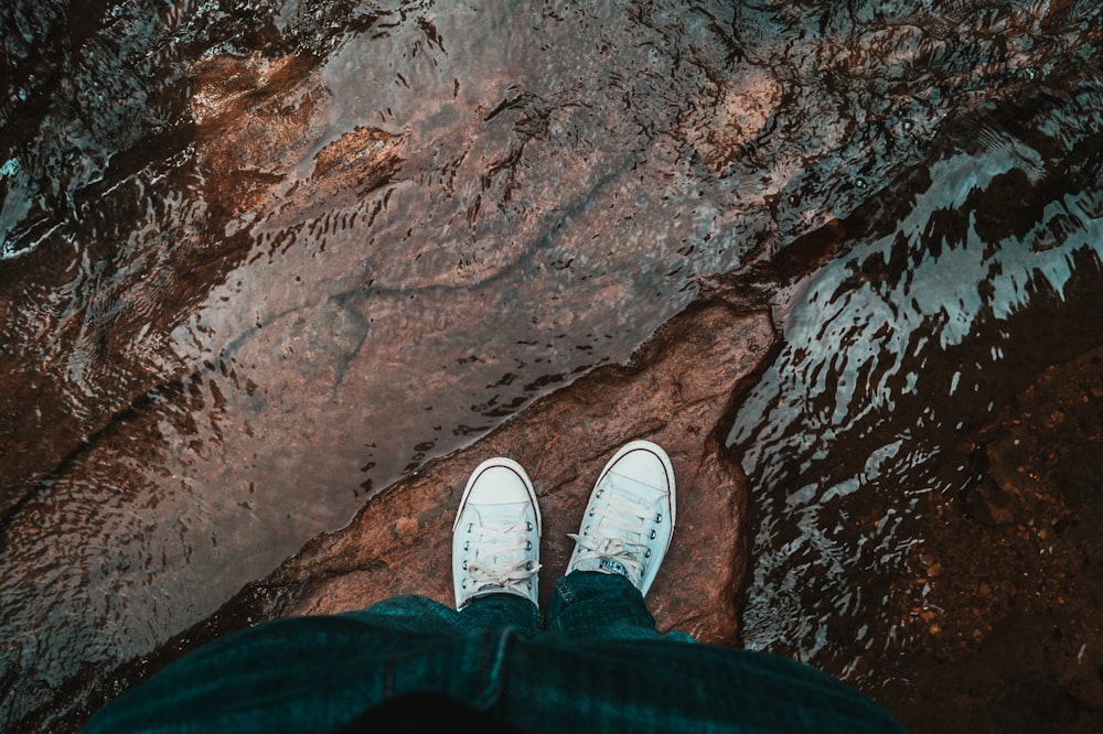 person in black pants and white sneakers standing on brown rock