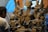 A sculptor works on a large clay statue depicting a multi-armed deity, surrounded by several smaller figures. The sculptures are in varying stages of completion, set against a rustic indoor backdrop with bluish light filtering through.