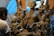 A sculptor works on a large clay statue depicting a multi-armed deity, surrounded by several smaller figures. The sculptures are in varying stages of completion, set against a rustic indoor backdrop with bluish light filtering through.