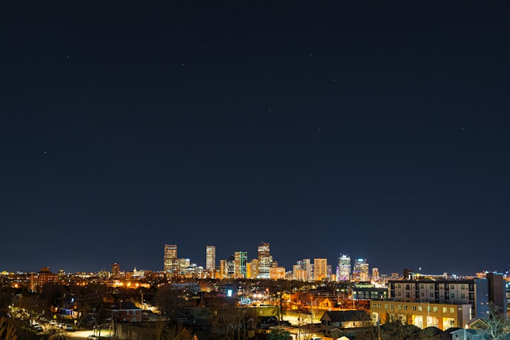 Denver skyline with the Rocky Mountains rising dramatically behind the city under a clear blue sky