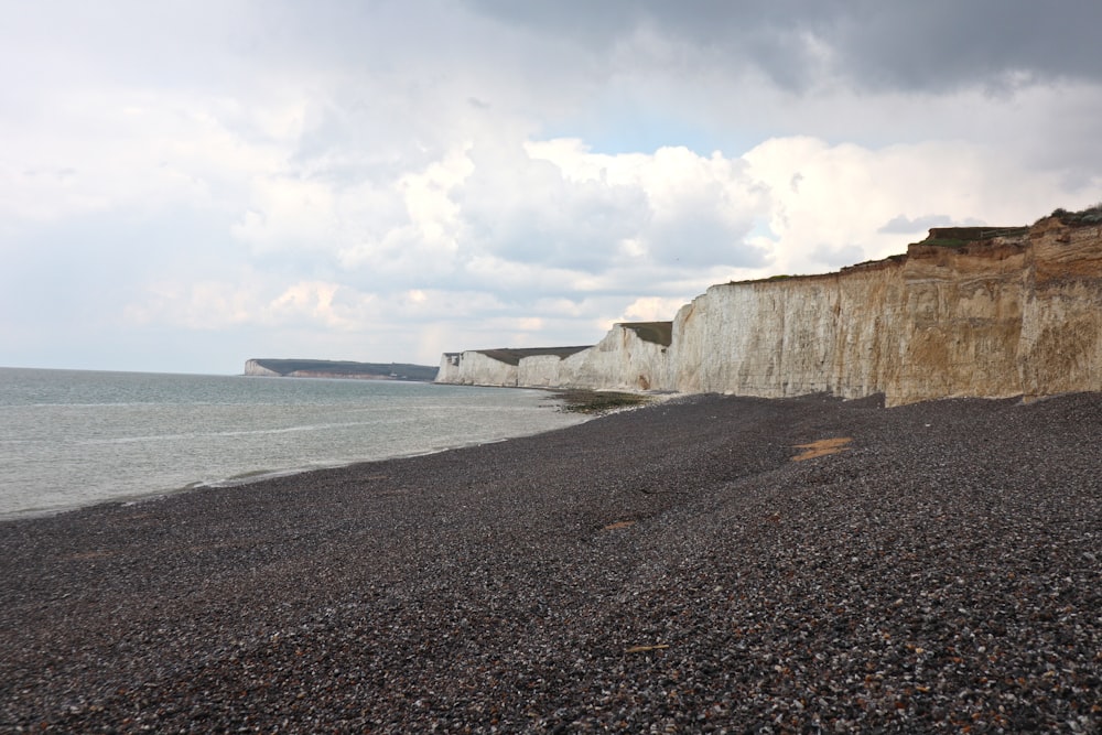 brown rocky mountain beside sea under white clouds and blue sky during daytime