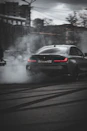 A close-up of an R34 GTR drifting under city lights with smoke swirling around its wheels.