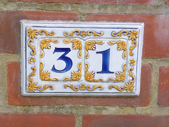 Laser-cut steel house number plate mounted on a garden wall surrounded by greenery.